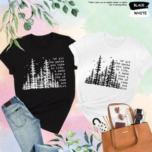 K&ouml;nnte beinhalten: Zwei T-Shirts mit einem schwarzen und wei&szlig;en Waldmotiv und dem Text 'of all the paths you take in life, make sure a few of them are dirt'. Die T-Shirts befinden sich auf einem rosa und wei&szlig;en Hintergrund.
