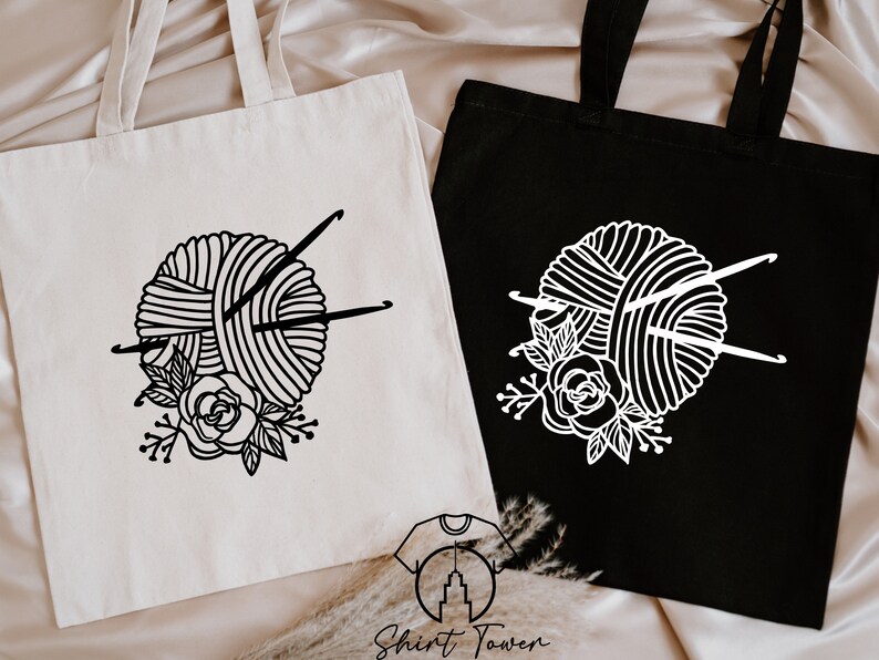 Pu&ograve; includere: Due borse tote con un designo in bianco e nero di un gomitolo di lana con ferri da maglia e un design floreale. La borsa a sinistra &egrave; bianca con un designo nero. La borsa a destra &egrave; nera con un designo bianco.