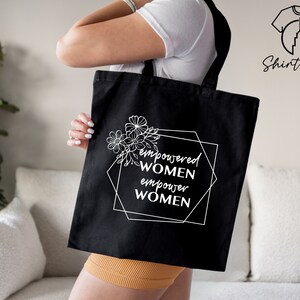 May include: Black tote bag with white text and floral design. The text reads "empowered women empower women".