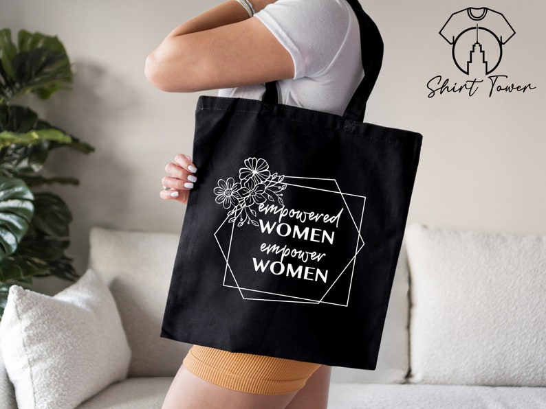 May include: Black tote bag with white text and floral design. The text reads "empowered women empower women".