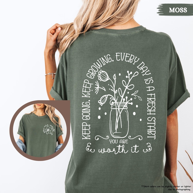 May include: A green t-shirt with a white graphic of a mason jar with flowers and the text "KEEP GOING. KEEP GROWING. EVERY DAY IS A FRESH START YOU ARE & worth it &"