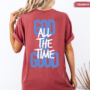 May include: Crimson-colored t-shirt with the text "GOD ALL THE TIME GOOD" in blue and white. The shirt has short sleeves and a relaxed fit. The word "CRIMSON" is in the upper right corner.