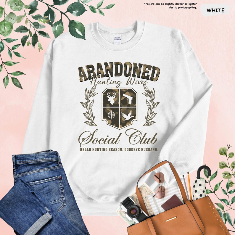 May include: White sweatshirt with the text "ABANDONED Hunting Wives Social Club" in a camouflage design. The design includes images of a deer, a gun, a target, and a bird. The phrase "HELLO HUNTING SEASON. GOODBYE HUSBAND." is also printed on the sweatshirt.
