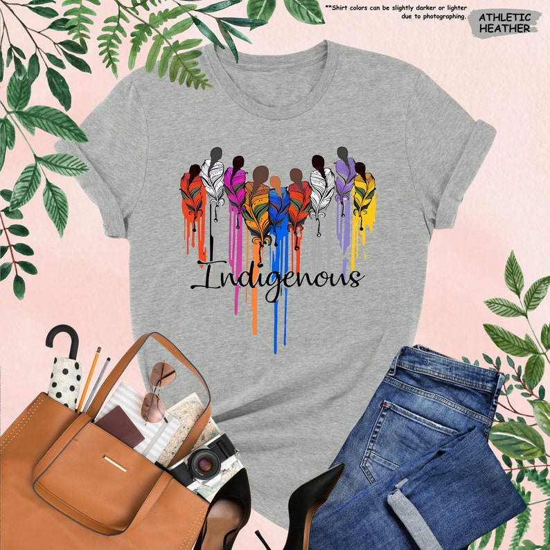 May include: Gray t-shirt with a colorful design of stylized figures with feathers and the word "Indigenous" in a dripping paint style.