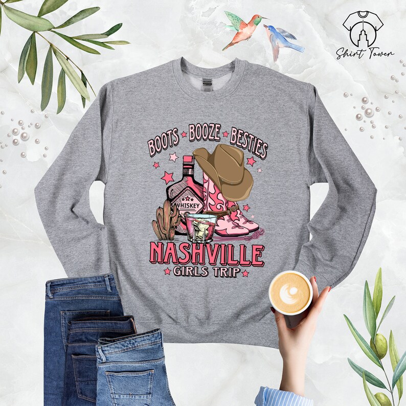 May include: Gray sweatshirt with a pink and brown graphic design that says "Boots Booze Besties Nashville Girls Trip". The graphic includes a bottle of whiskey, a shot glass, and cowboy boots.
