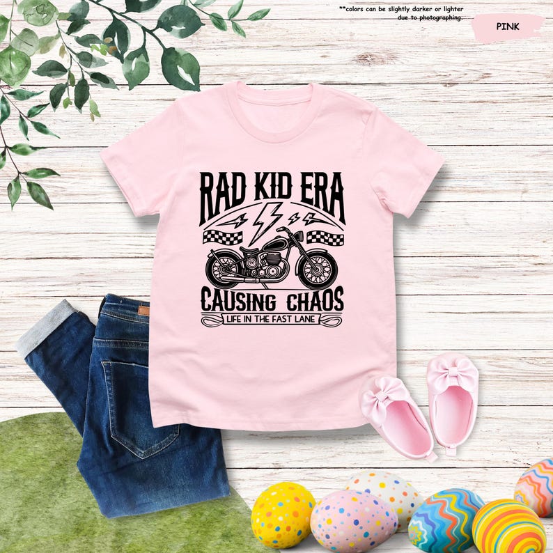 May include: Pink t-shirt with a black and white graphic of a motorcycle with the text "Rad Kid Era Causing Chaos Life in the Fast Lane"