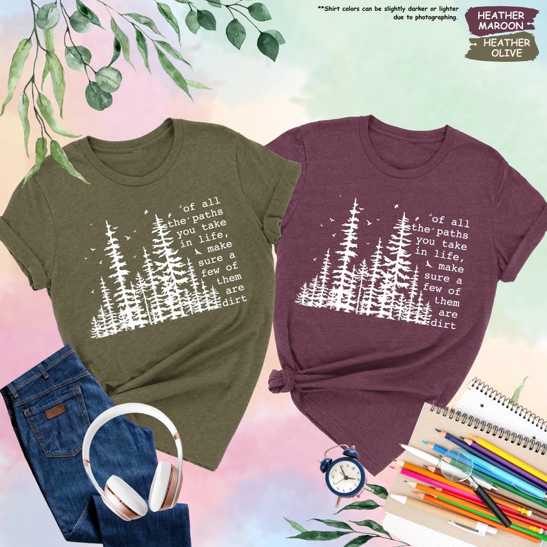 K&ouml;nnte beinhalten: Zwei T-Shirts mit einer Waldszene und dem Text "of all the' paths you take in life, make sure a few of them are dirt". Das T-Shirt links ist olivgr&uuml;n und das T-Shirt rechts ist dunkelrot.