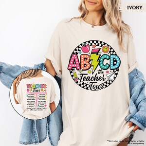 May include: A white t-shirt with a colorful graphic design featuring the letters ABCD, a lightning bolt, and the text "the Teacher Tour".