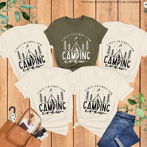 Peut inclure: Quatre t-shirts cr&egrave;me avec du texte noir qui dit "Fires, Friends, Fun, Camping Crew" et un graphique d'un feu de camp et d'une tente. Un t-shirt est de couleur vert fonc&eacute;.