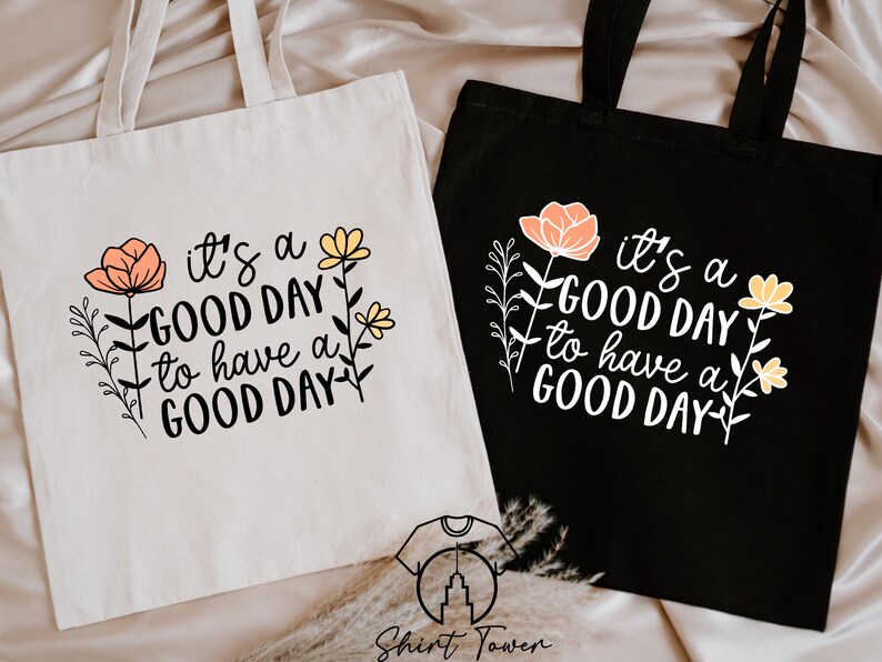 May include: Two tote bags with the text "it's a GOOD DAY to have a GOOD DAY" printed on them. The bags are made of canvas and have floral designs. One bag is white and the other is black.