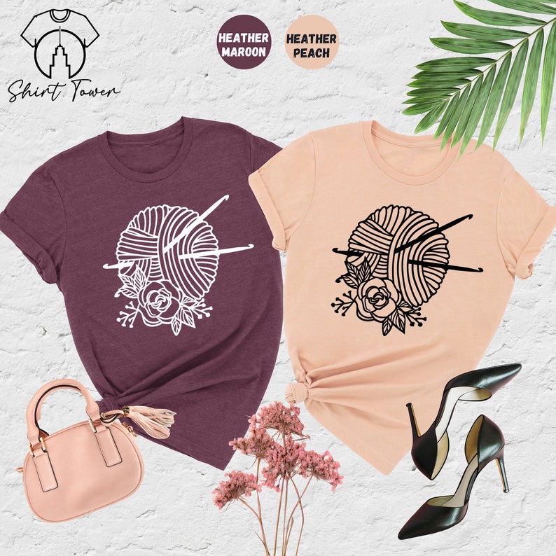 Pode incluir: Duas camisetas com um design de novelo de l&atilde; e agulhas de tric&ocirc;. A camiseta &agrave; esquerda &eacute; de cor marrom mesclada e a camiseta &agrave; direita &eacute; de cor p&ecirc;ssego mesclada. Shirt Town.