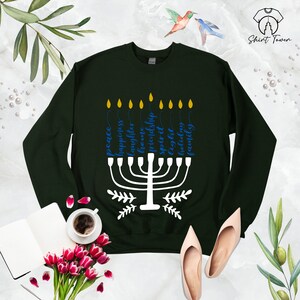 Puede incluir: Una sudadera de color verde oscuro con un dise&ntilde;o de menor&aacute; blanco y texto azul que dice "paz, felicidad, risa, amor, amistad, esp&iacute;ritu, especial, luz, vacaciones, familia".