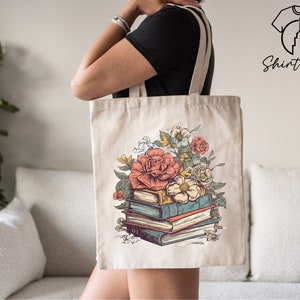 May include: A white canvas tote bag with a floral design and a stack of books. The flowers are pink, red, and white. The books are brown, blue, and green.