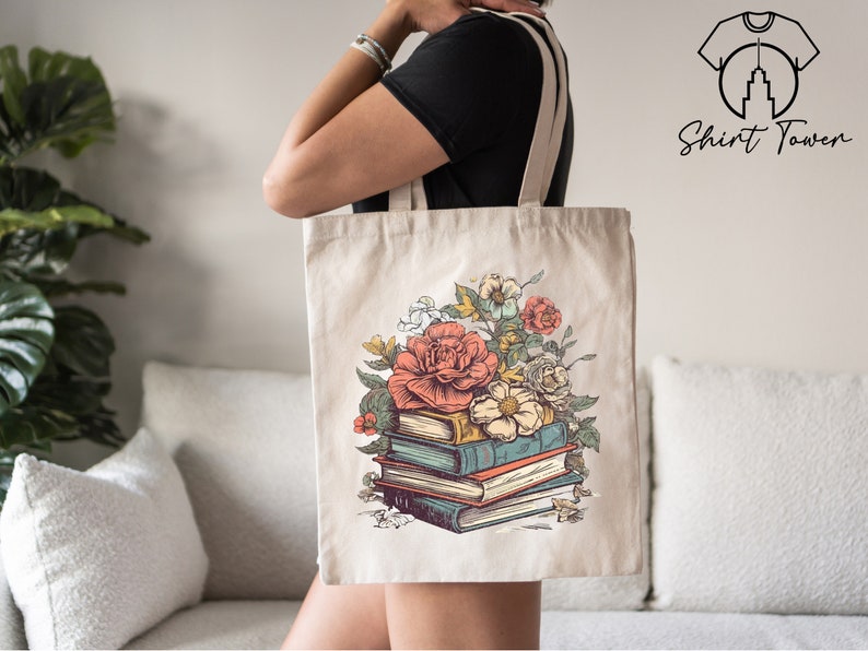 May include: A white canvas tote bag featuring a floral design and a stack of books. The flowers are pink, red, and white. The books are brown, blue, and green.