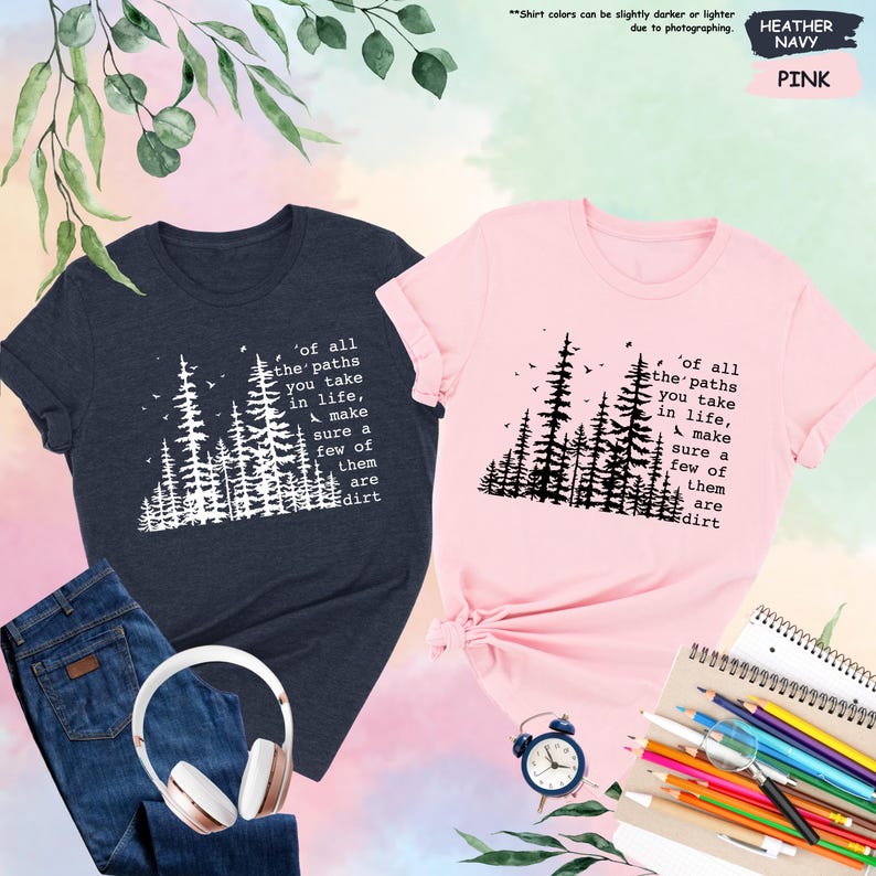 K&ouml;nnte beinhalten: Zwei T-Shirts mit einer Waldszene und dem Text 'of all the paths you take in life, make sure a few of them are dirt'. Das Shirt links ist marineblau und das Shirt rechts ist rosa.