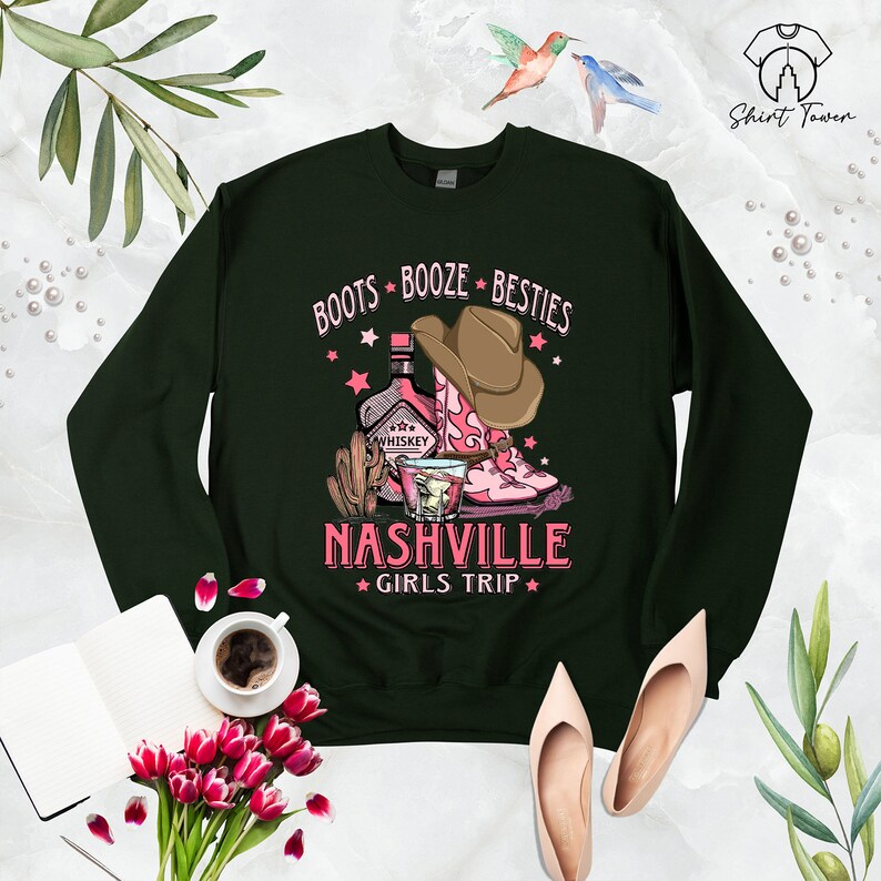 May include: Green sweatshirt with a pink graphic design that says "Boots Booze Besties Nashville Girls Trip". The graphic features a bottle of whiskey, a glass of whiskey, and a pair of pink cowboy boots.