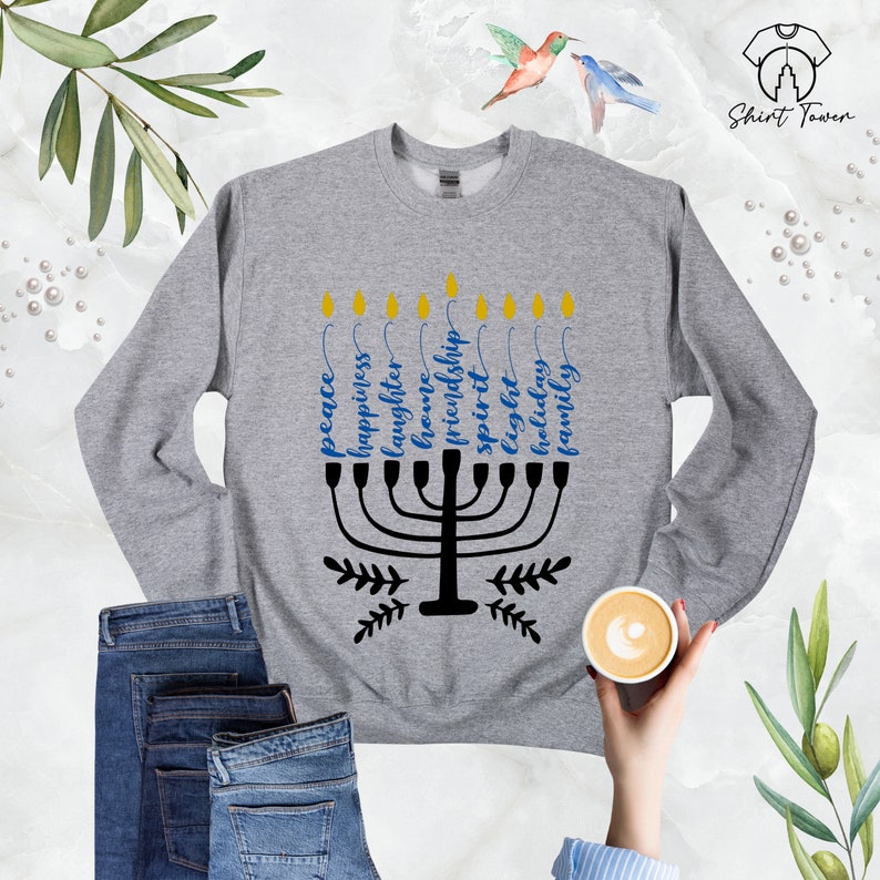 Puede incluir: Una sudadera gris con un dise&ntilde;o de menor&aacute; negro y las palabras "paz", "felicidad", "risa", "amor", "hogar", "amistad", "esp&iacute;ritu", "luz", "vacaciones" y "familia" escritas alrededor.