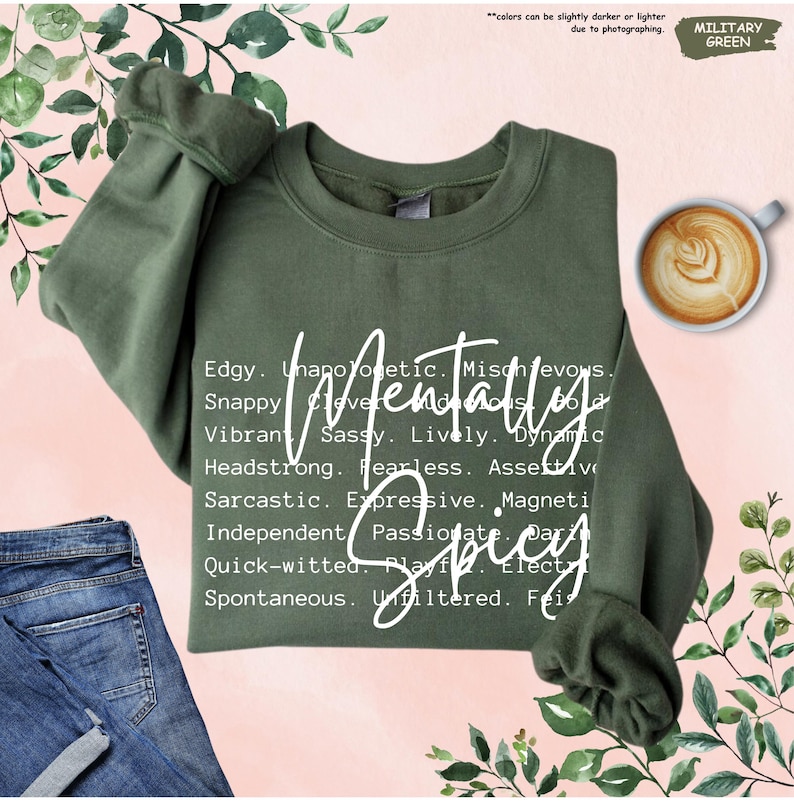 May include: Military green sweatshirt with the word "Mentally Spicy" in white script. The sweatshirt features a crew neck and long sleeves. Additional words describing personality traits are printed below the main text.