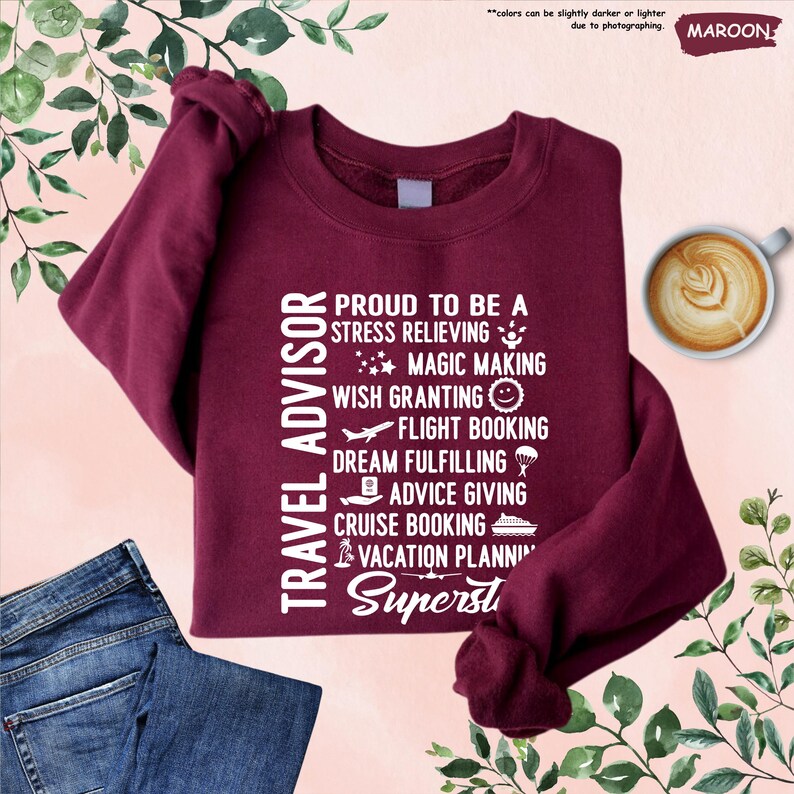 May include: A maroon sweatshirt with white text that reads "Travel Advisor" and lists the duties of a travel advisor, including "stress relieving", "magic making", "wish granting", "flight booking", "dream fulfilling", "advice giving", "cruise booking", and "vacation planning". The text ends with the word "Superst".