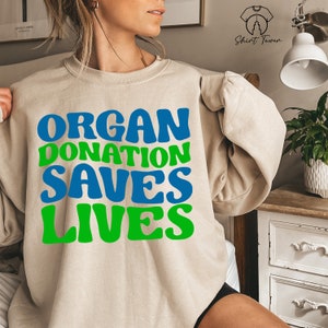 May include: A beige sweatshirt with the text "ORGAN DONATION SAVES LIVES" in green and blue letters.