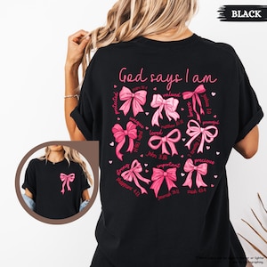 K&ouml;nnte beinhalten: Schwarzes T-Shirt mit einem rosa und wei&szlig;en Design, auf dem "Gott sagt, ich bin" steht, mit einem Kreis aus rosa Schleifen und Bibelversen um die Worte.