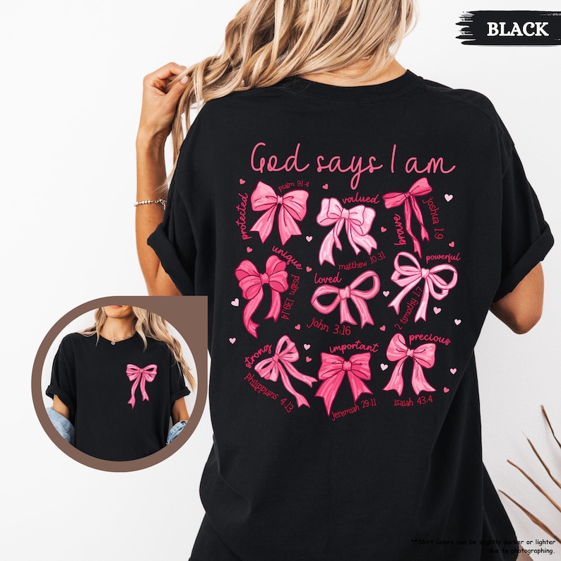 K&ouml;nnte beinhalten: Schwarzes T-Shirt mit einem rosa und wei&szlig;en Design, auf dem "Gott sagt, ich bin" steht, mit einem Kreis aus rosa Schleifen und Bibelversen um die Worte.