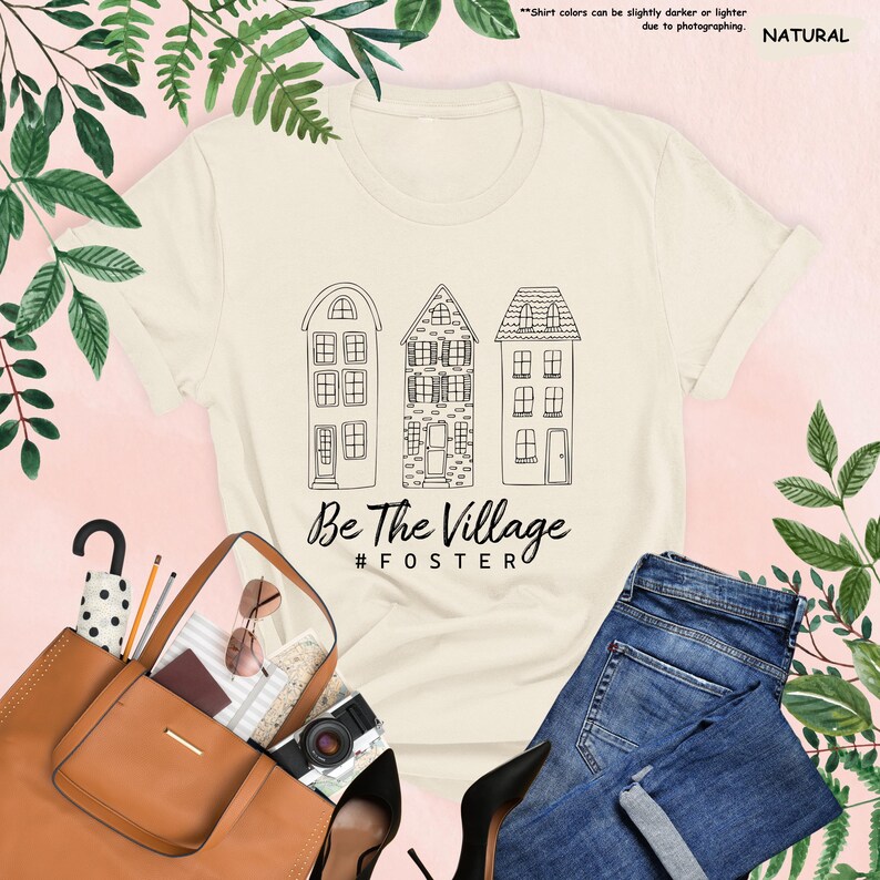 May include: A beige t-shirt with a black graphic of three houses and the text "Be The Village #FOSTER".