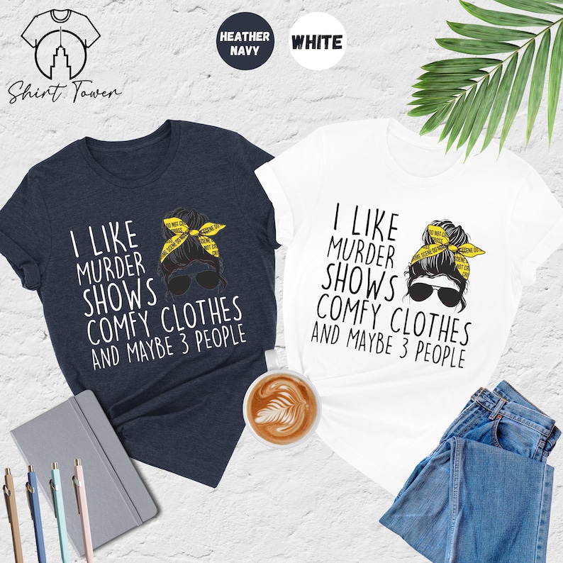 May include: Two t-shirts with a graphic of a woman with a messy bun and sunglasses. The text on the shirts reads "I like murder shows comfy clothes and maybe 3 people". The shirts are available in heather navy and white.