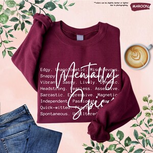 May include: Maroon sweatshirt with the words "Mentally Spicy" in white script. The sweatshirt has a crew neck and long sleeves. A cup of coffee and a pair of blue jeans are also in the image.
