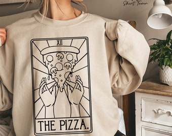 Könnte beinhalten: Ein beiger Pullover mit einer schwarz-weißen Illustration einer Pizzastückes mit dem Text "The Pizza" und "XII" darauf.