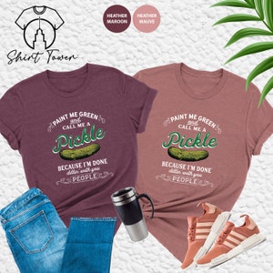 May include: Two t-shirts with a pickle graphic and the text "Paint me green and call me a pickle because I'm done dillin' with you people". The shirts are available in heather maroon and heather mauve.
