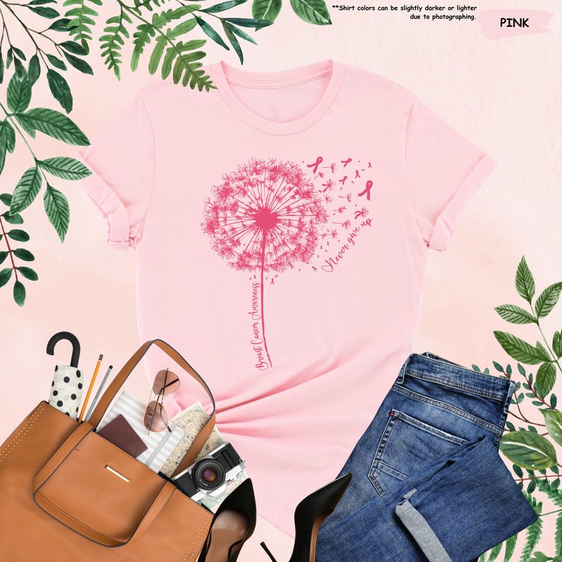 Puede incluir: Una camiseta rosa con un dise&ntilde;o de diente de le&oacute;n rosa, con las palabras "Breast Cancer Awareness" y "Never give up". La camiseta se combina con vaqueros azules, un bolso marr&oacute;n y tacones negros.