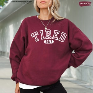 a woman wearing a maroon sweatshirt with the word tired on it