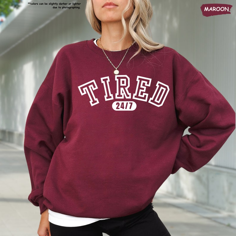 a woman wearing a maroon sweatshirt with the word tired on it
