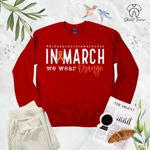 Puede incluir: Sudadera roja de manga larga con el texto "#kidneycancerawareness IN MARCH we wear Orange" y una cinta naranja.