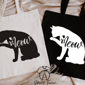 Op de afbeelding: Twee tote bags met een zwart kat silhouet en het woord "Meow" op een witte tas en een wit kat silhouet en het woord "Meow" op een zwarte tas.