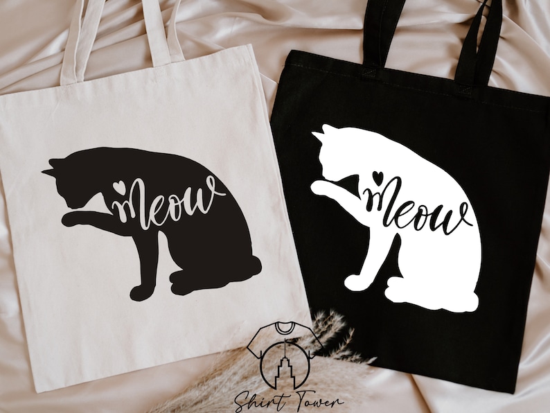 Op de afbeelding: Twee tote bags met een zwart kat silhouet en het woord "Meow" op een witte tas en een wit kat silhouet en het woord "Meow" op een zwarte tas.