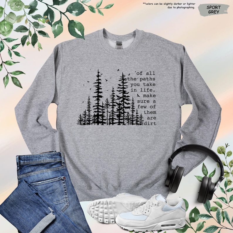K&ouml;nnte beinhalten: Ein graues Sweatshirt mit einer schwarzen Silhouette eines Waldes und dem Text 'of all the paths you take in life, make sure a few of them are dirt'.