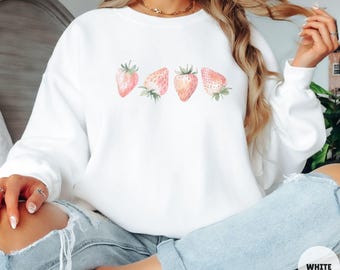 May include: White sweatshirt with a watercolor design of five pink strawberries. The strawberries are arranged in a row across the front of the sweatshirt.
