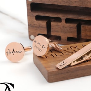 May include: Rose gold cufflinks and tie clip set in a wooden box. The cufflinks are engraved with the names "Andrew" and "A&C" and the date "26.09.2023". The tie clip is engraved with "A&C" and the date "26.09.2023".