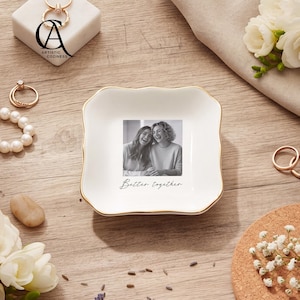 May include: A square white ceramic trinket dish with scalloped edges and a gold-toned rim. The center features a black and white photograph of two smiling individuals with the printed text Better together below the image in a cursive script.