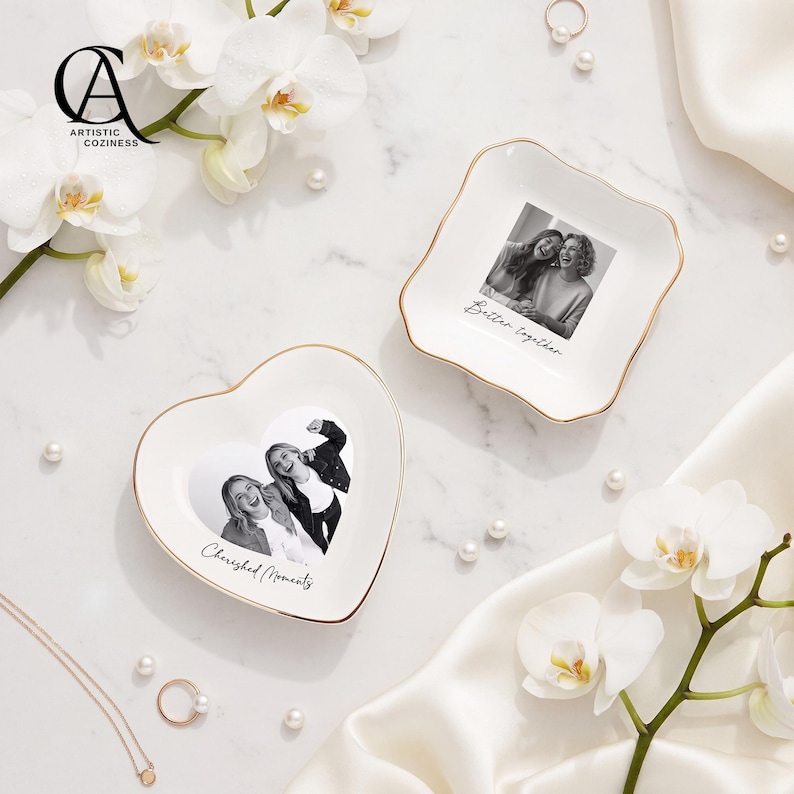 May include: Two white ceramic trinket dishes with gold-toned rims. One dish is heart-shaped with a black and white photo and the text Cherished Moments. The other is square with rounded corners, a black and white photo, and the text Better together.