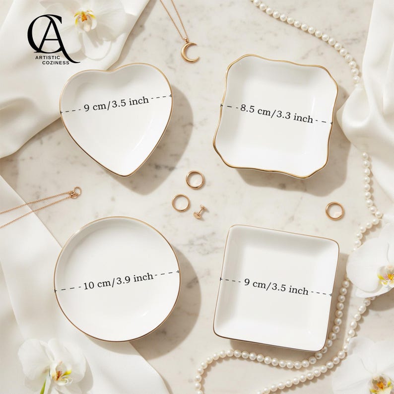 May include: Four white ceramic trinket dishes with gold-painted rims in heart, square, and round shapes. The heart dish is 3.5 inches wide, the square dish with wavy edges is 3.3 inches, the round dish is 3.9 inches, and the square dish is 3.5 inches.