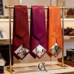 May include: Three satin neckties in deep red, magenta, and bright orange hanging on a gold metal display stand. Each tie features a diamond-shaped cutout at the bottom displaying a different color photograph of people and a dog.