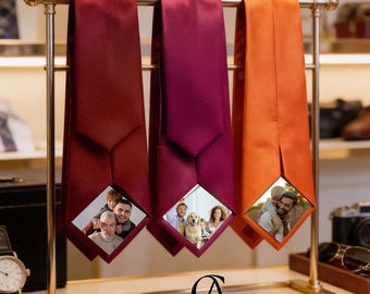 May include: Three satin neckties in deep red, magenta, and bright orange hanging on a gold metal display stand. Each tie features a diamond-shaped cutout at the bottom displaying a different colour photograph of people and a dog.