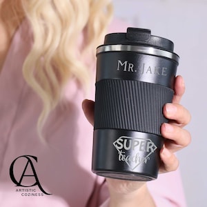 May include: Black travel mug with a silver lid and a silver band around the middle. The mug has the text "Mr. Jake" and "Super Teacher" engraved on it.