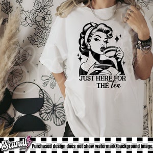May include: White t-shirt featuring a black and white graphic of a woman drinking tea, with the text "JUST HERE FOR THE tea". The design has a vintage aesthetic with star accents.