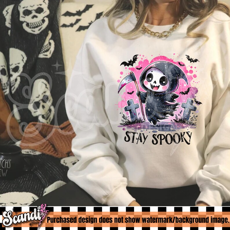 May include: White sweatshirt featuring a cartoon grim reaper with a scythe, surrounded by bats and tombstones. The phrase "STAY SPOOKY" is printed below the graphic. The design has pink and purple watercolor accents, perfect for Halloween.