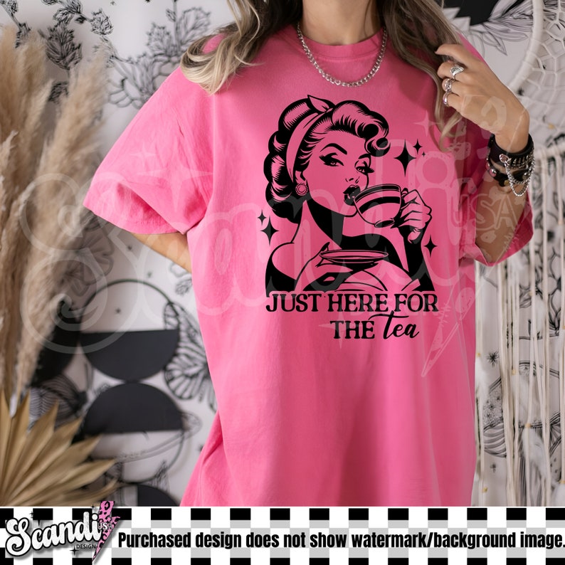 May include: A bright pink t-shirt featuring a black and white graphic of a woman drinking tea, with the text "JUST HERE FOR THE tea". The shirt has short sleeves and a relaxed fit.