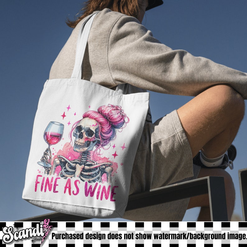 K&ouml;nnte beinhalten: Wei&szlig;e Einkaufstasche mit einem rosa und wei&szlig;en Skelett, das ein Glas Rotwein h&auml;lt. Der Text "FINE AS WINE" ist auf die Tasche gedruckt.